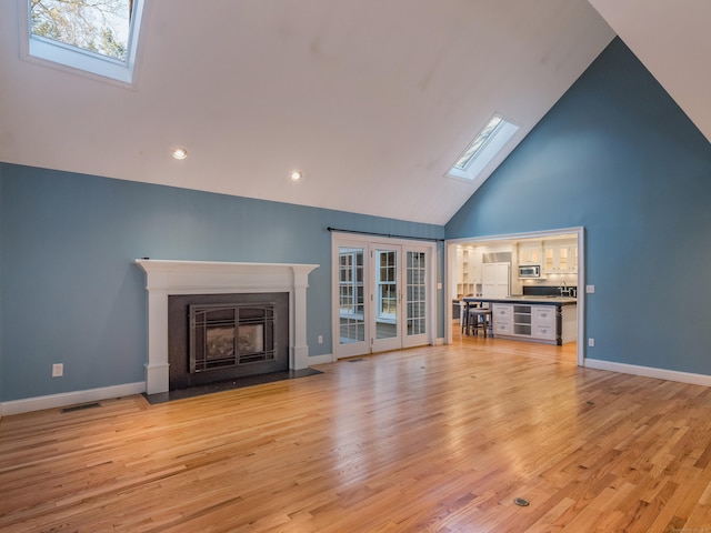 unfurnished living room featuring high vaulted ceiling, light wood-type flooring, and a skylight