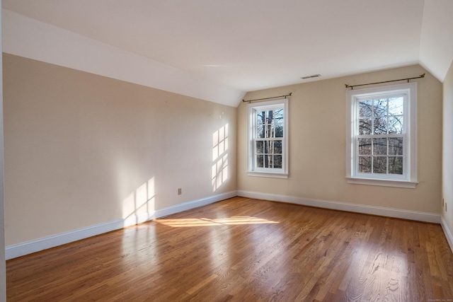 empty room featuring lofted ceiling, hardwood / wood-style floors, and plenty of natural light