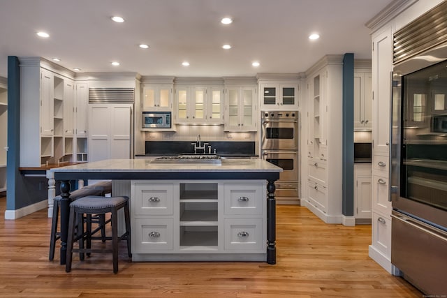 kitchen with white cabinetry, light stone counters, a kitchen bar, an island with sink, and appliances with stainless steel finishes