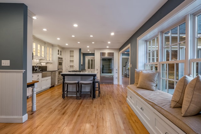 kitchen with white cabinets, a kitchen breakfast bar, light hardwood / wood-style flooring, a kitchen island, and appliances with stainless steel finishes