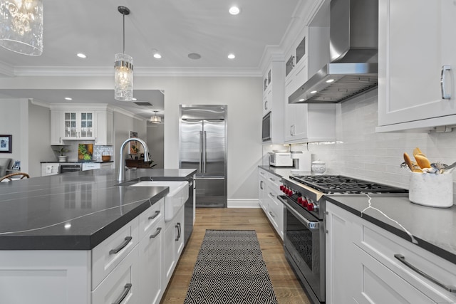 kitchen featuring white cabinetry, a large island, wall chimney exhaust hood, built in appliances, and pendant lighting