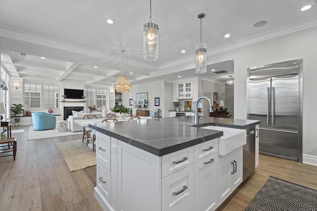 kitchen with stainless steel built in refrigerator, beam ceiling, a center island with sink, decorative light fixtures, and white cabinets