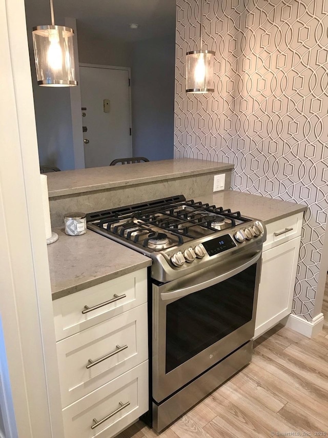 kitchen with pendant lighting, white cabinets, light hardwood / wood-style flooring, and stainless steel gas range oven