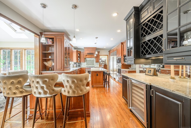 kitchen featuring a center island, wine cooler, decorative backsplash, light stone countertops, and a breakfast bar area