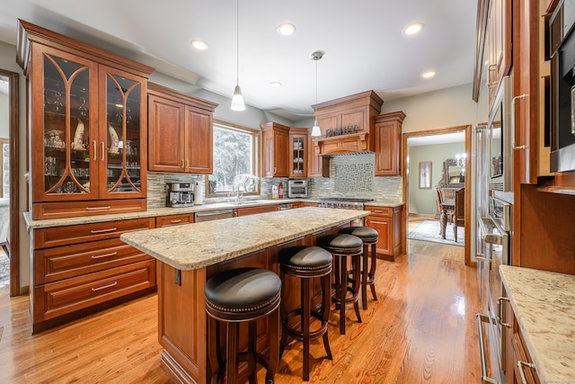 kitchen with a center island, stainless steel appliances, pendant lighting, decorative backsplash, and light wood-type flooring