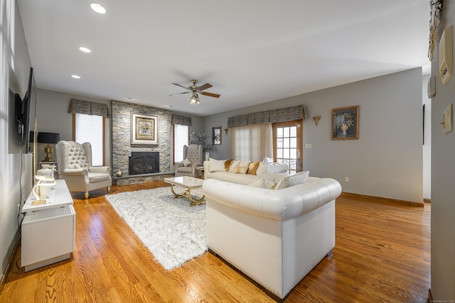 living room with hardwood / wood-style floors, a stone fireplace, and ceiling fan