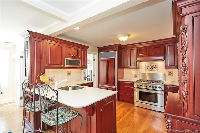 kitchen featuring range hood, a breakfast bar, sink, built in appliances, and light hardwood / wood-style flooring