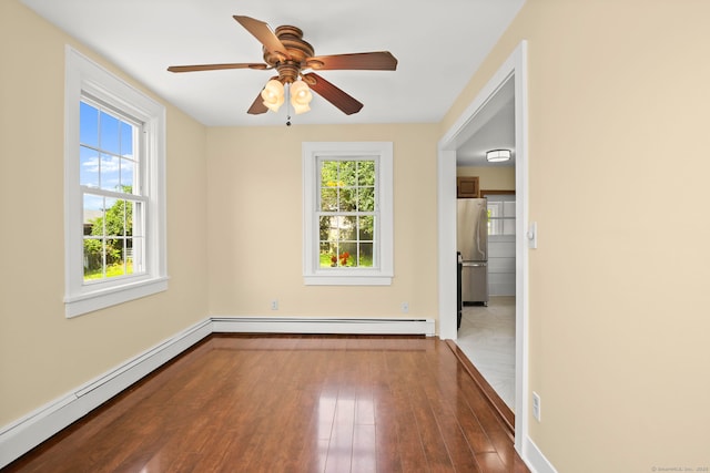 empty room featuring hardwood / wood-style flooring, ceiling fan, a healthy amount of sunlight, and baseboard heating