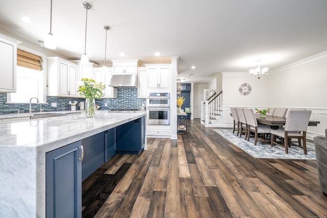 kitchen featuring a kitchen island, white cabinetry, hanging light fixtures, blue cabinetry, and stainless steel double oven