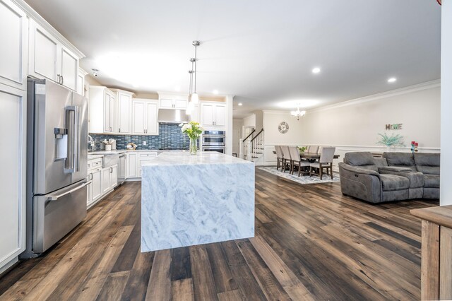 kitchen with decorative light fixtures, white cabinetry, a center island, light stone counters, and stainless steel appliances