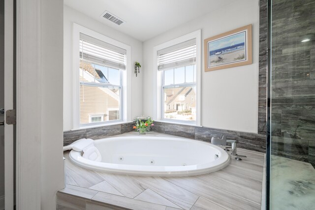 bathroom with a healthy amount of sunlight and tiled bath