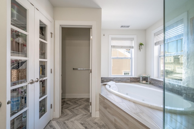 bathroom featuring a relaxing tiled tub, parquet floors, and french doors