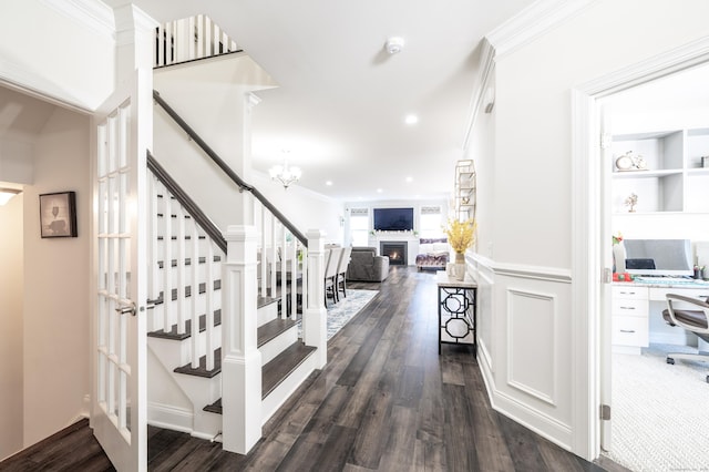 hallway with dark wood finished floors, stairs, wainscoting, crown molding, and a decorative wall