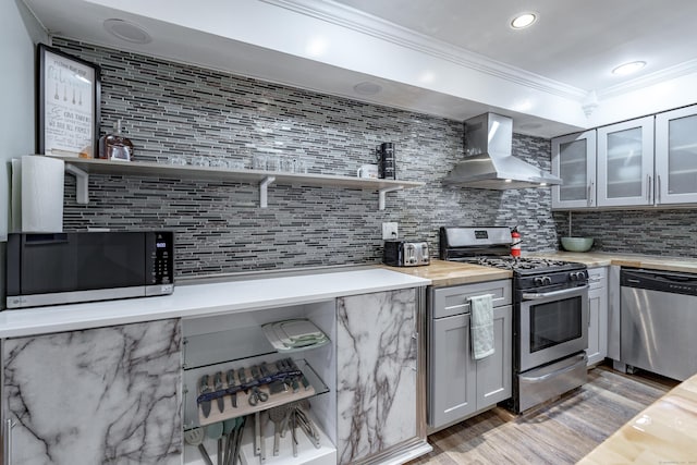 kitchen with butcher block countertops, decorative backsplash, ornamental molding, stainless steel appliances, and wall chimney exhaust hood