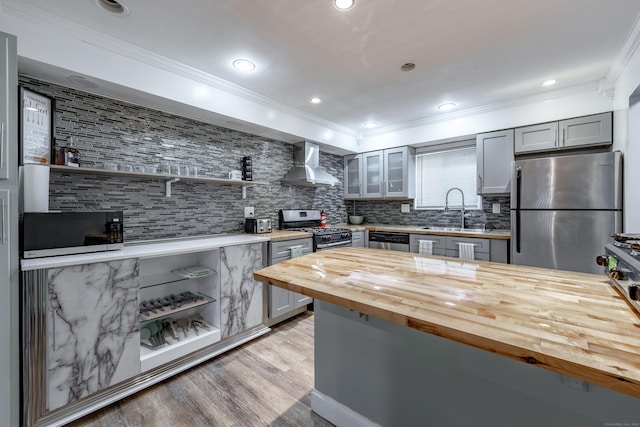 kitchen with appliances with stainless steel finishes, sink, gray cabinetry, wooden counters, and wall chimney exhaust hood