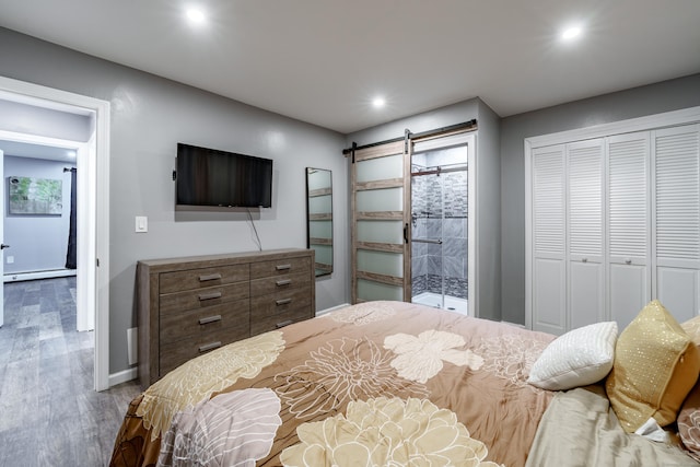 bedroom with hardwood / wood-style flooring, a barn door, a baseboard heating unit, and a closet