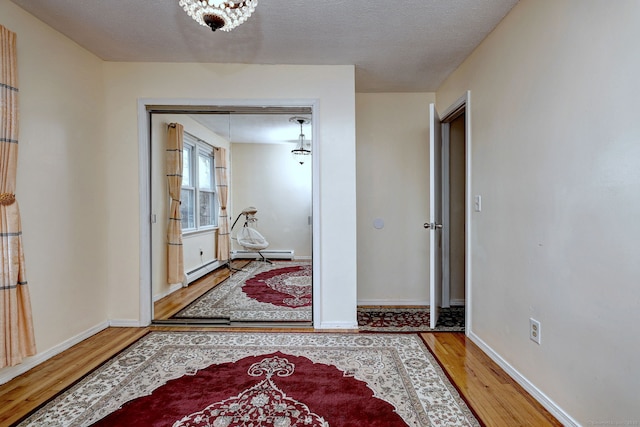 hallway with wood-type flooring, a textured ceiling, and a baseboard heating unit