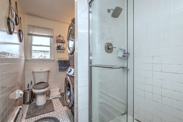 bathroom featuring stacked washing maching and dryer, baseboard heating, a shower with door, tile walls, and toilet