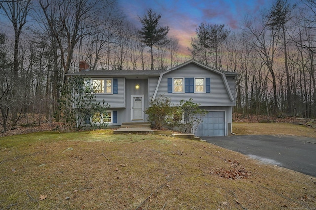 raised ranch featuring a garage and a lawn