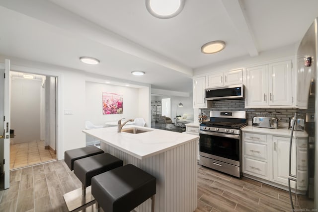 kitchen with white cabinetry, sink, stainless steel appliances, an island with sink, and a breakfast bar