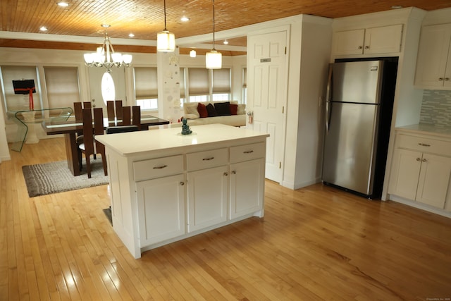 kitchen featuring stainless steel refrigerator, white cabinets, and hanging light fixtures