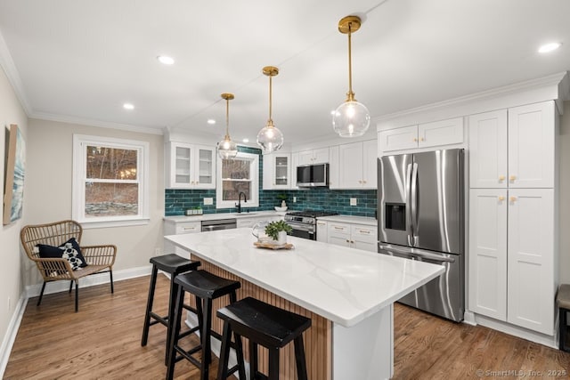 kitchen featuring light stone counters, stainless steel appliances, pendant lighting, a center island, and white cabinetry