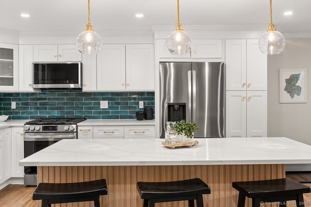 kitchen with a kitchen bar, light stone counters, stainless steel appliances, a kitchen island, and white cabinetry