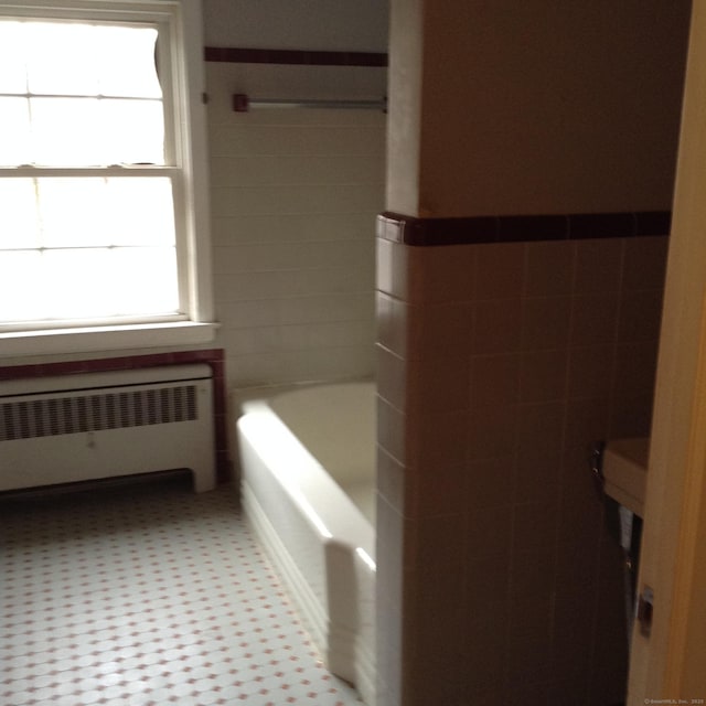 bathroom featuring radiator, tile walls, and a tub to relax in