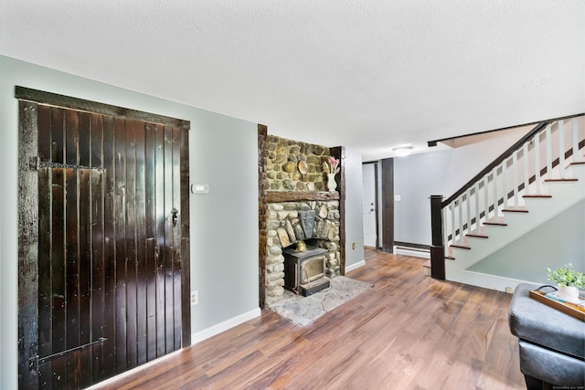 living room with a textured ceiling, a wood stove, wood-type flooring, and a baseboard radiator