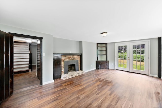 unfurnished living room featuring dark hardwood / wood-style floors, french doors, and a brick fireplace