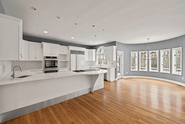 kitchen featuring appliances with stainless steel finishes, sink, light stone counters, light wood-type flooring, and white cabinetry