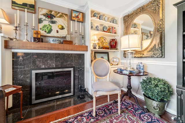 living area featuring hardwood / wood-style flooring, built in features, ornamental molding, and a tiled fireplace