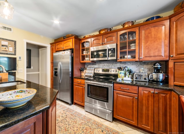 kitchen with dark stone countertops, decorative backsplash, light tile patterned flooring, and appliances with stainless steel finishes