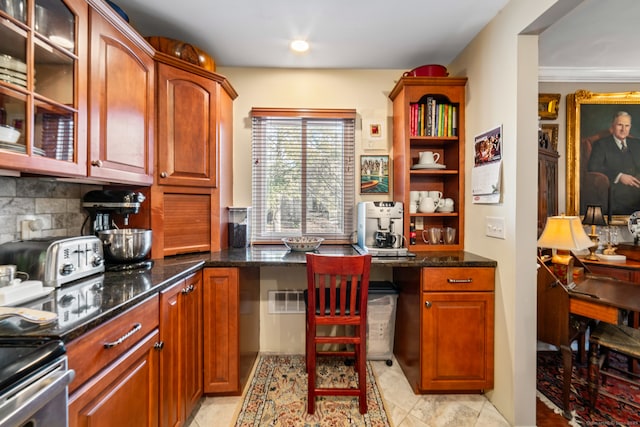 kitchen with stainless steel electric range, built in desk, backsplash, and dark stone counters