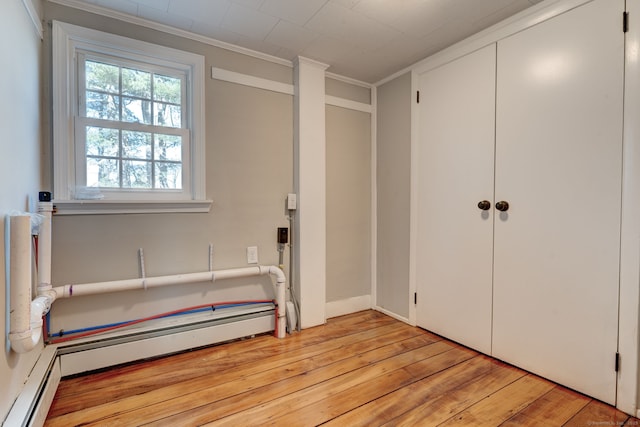 unfurnished bedroom featuring a baseboard heating unit, crown molding, and light wood-type flooring