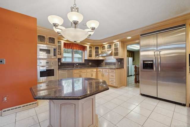 kitchen with a baseboard radiator, hanging light fixtures, built in appliances, a kitchen island, and sink