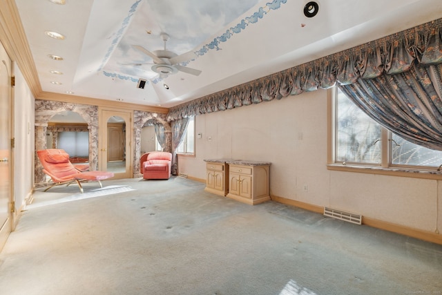 interior space with ceiling fan, a wealth of natural light, ornamental molding, and a raised ceiling