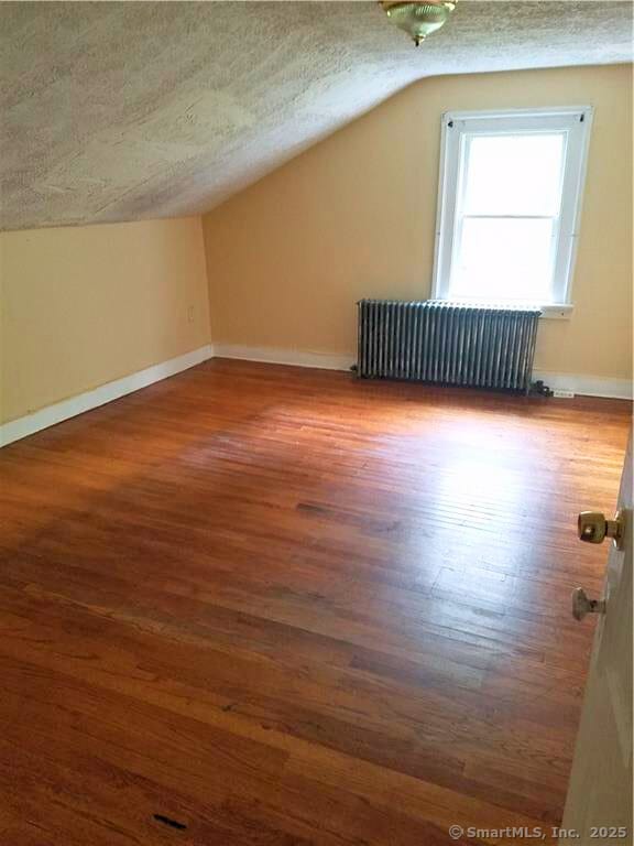 bonus room with a textured ceiling, lofted ceiling, radiator heating unit, and dark wood-type flooring