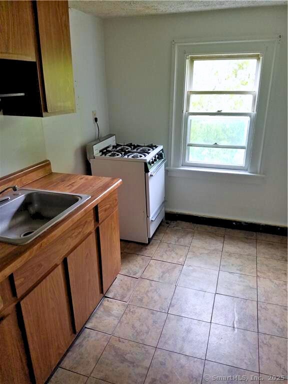 kitchen featuring white range with gas cooktop, sink, light tile patterned floors, and a textured ceiling