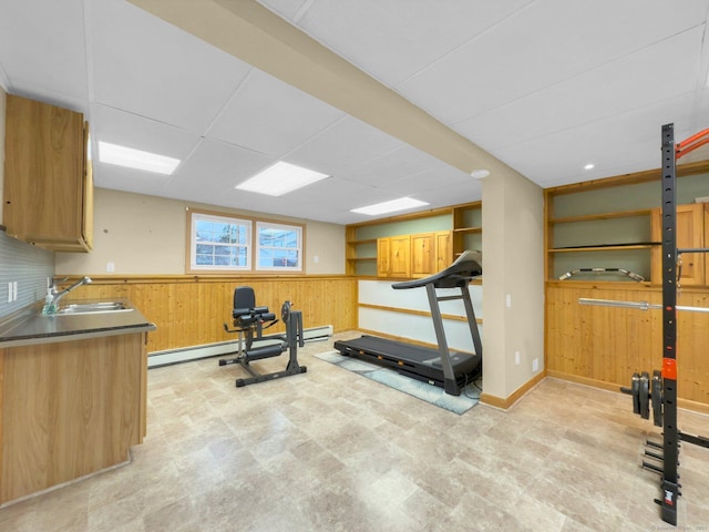 exercise area with sink, a baseboard radiator, wood walls, and a paneled ceiling