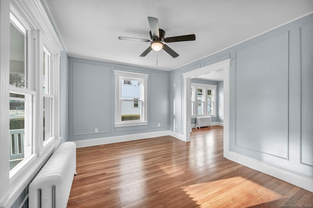 empty room with radiator, ceiling fan, wood-type flooring, and ornamental molding