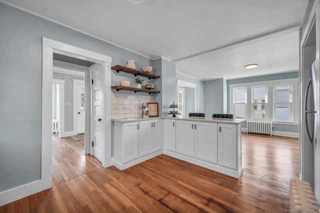 kitchen with radiator heating unit, light hardwood / wood-style flooring, backsplash, kitchen peninsula, and white cabinets