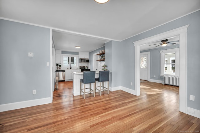 kitchen with radiator, ceiling fan, stainless steel appliances, a breakfast bar area, and white cabinets