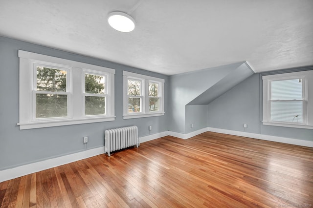 additional living space with hardwood / wood-style floors, radiator, and vaulted ceiling