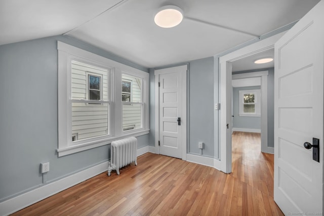 interior space featuring vaulted ceiling, radiator heating unit, plenty of natural light, and light wood-type flooring