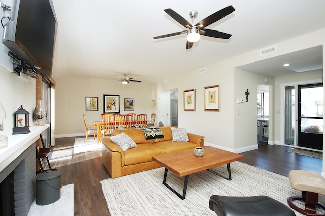 living room featuring dark wood-type flooring, a brick fireplace, and ceiling fan