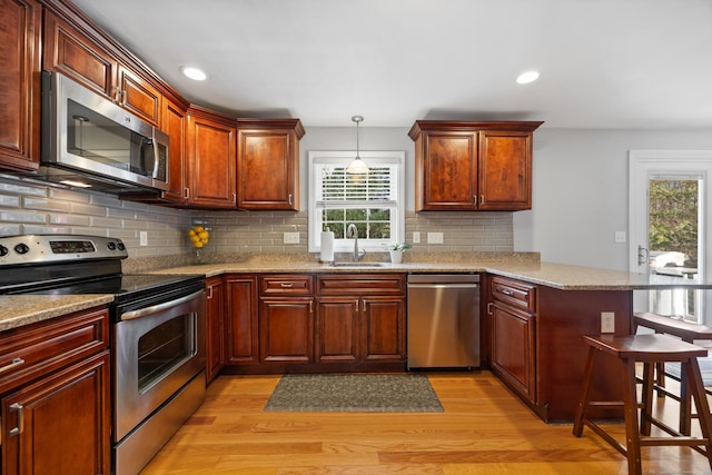 kitchen with a kitchen breakfast bar, sink, hanging light fixtures, kitchen peninsula, and stainless steel appliances