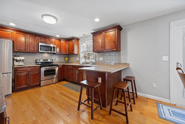 kitchen with sink, stainless steel appliances, kitchen peninsula, pendant lighting, and a breakfast bar area