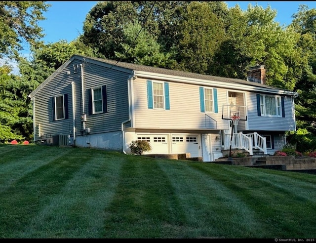 raised ranch with cooling unit, a garage, and a front lawn