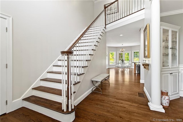 stairs with decorative columns, crown molding, hardwood / wood-style floors, and an inviting chandelier